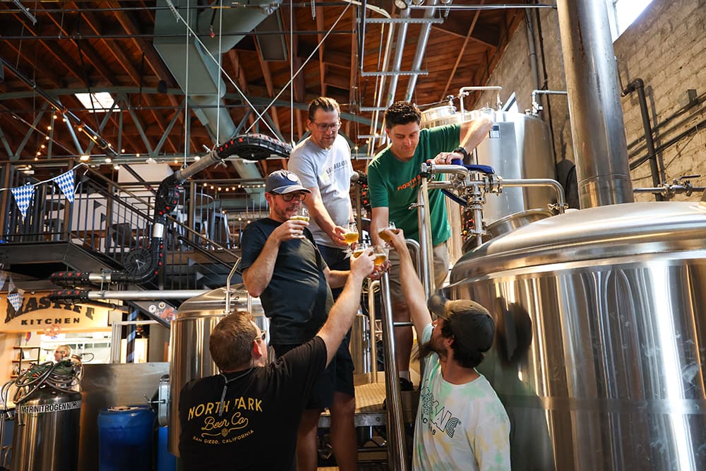 North Park Beer Company team toasts next to a large tank.